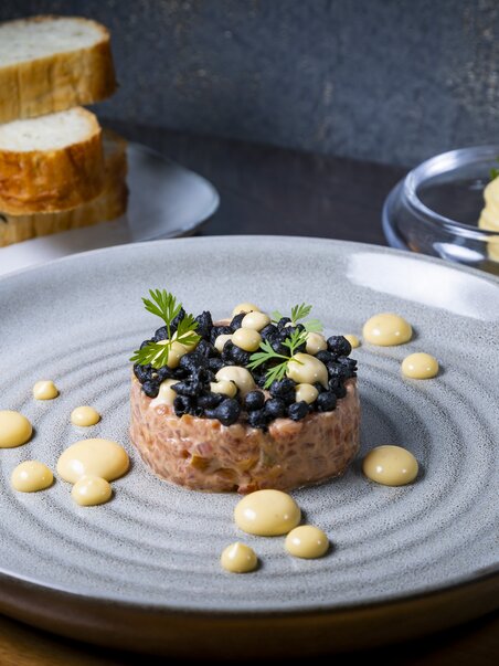 A plate of tartare, blueberries and sauces, enriched with fresh herbs. Fresh bread in the background. | © Graz Tourismus - Werner Krug
