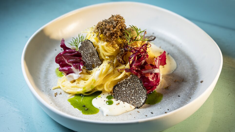 Un piatto di pasta decorato con tartufo, radicchio e salsa cremosa su un piatto chiaro. | © Graz Tourismus - Werner Krug