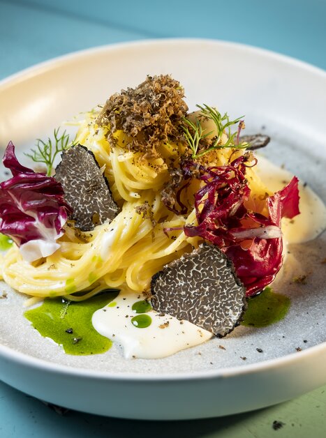 Ein kunstvoll angerichtetes Pastagericht mit Trüffeln, Radicchio und cremiger Sauce auf einem hellen Teller. | © Graz Tourismus - Werner Krug
