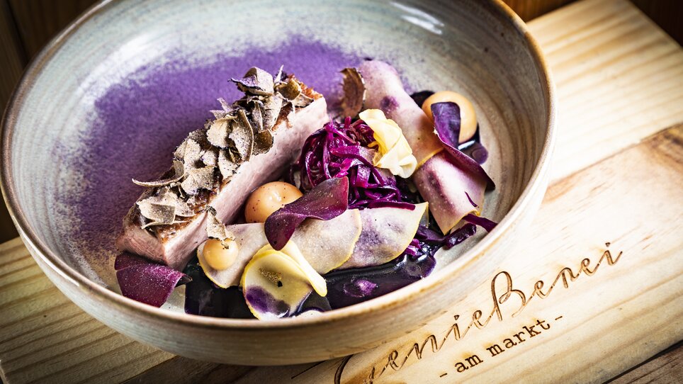 Ein kunstvolles Gericht mit Trüffeln, lila Rotkohl und Gemüse an einem Holzbrett mit Inschrift. | © Graz Tourismus - Werner Krug