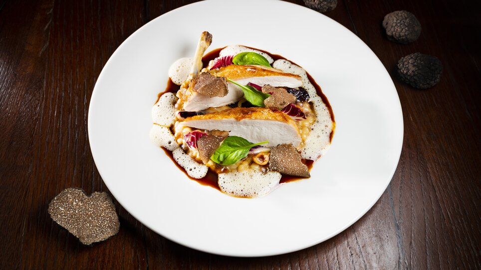 Ein kunstvoll angerichtetes Gericht mit Geflügel, Trüffeln und einer Soße auf einem weissen Teller. | © Graz Tourismus - Werner Krug