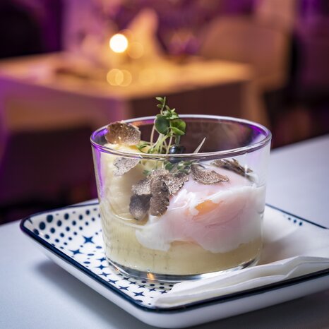 A glass with a fine dish of puree, a poached egg, and truffle slices, served on a plate. | © Graz Tourismus - Werner Krug