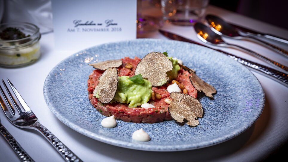 Ein kunstvoll angerichtetes Steak-Tatar mit Avocado, Trüffeln und Saucen auf einem blauen Teller. | © Graz Tourismus - Werner Krug