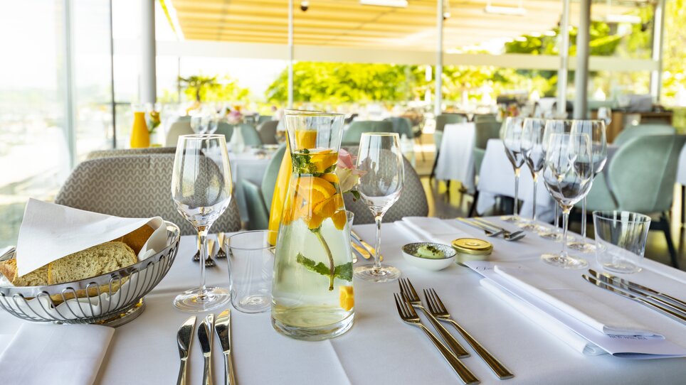 Elegant restaurant setup with glasses, a pitcher of water with lemons and fresh herbs, and fresh bread. | © Werner Krug