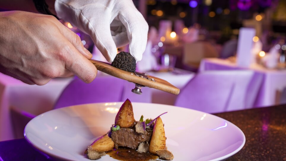 Ein Kellner mit weißen Handschuhen serviert ein Gericht und reibt frischen Trüffel darüber. | © Werner Krug