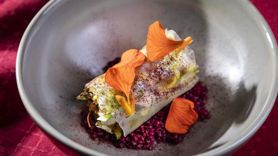 Ein kunstvolles Gericht mit einer gefüllten Rolle, bunten Blüten und einer bunten Quinoa-Basis, serviert in einer Schüssel. | © Graz Tourismus - Werner Krug