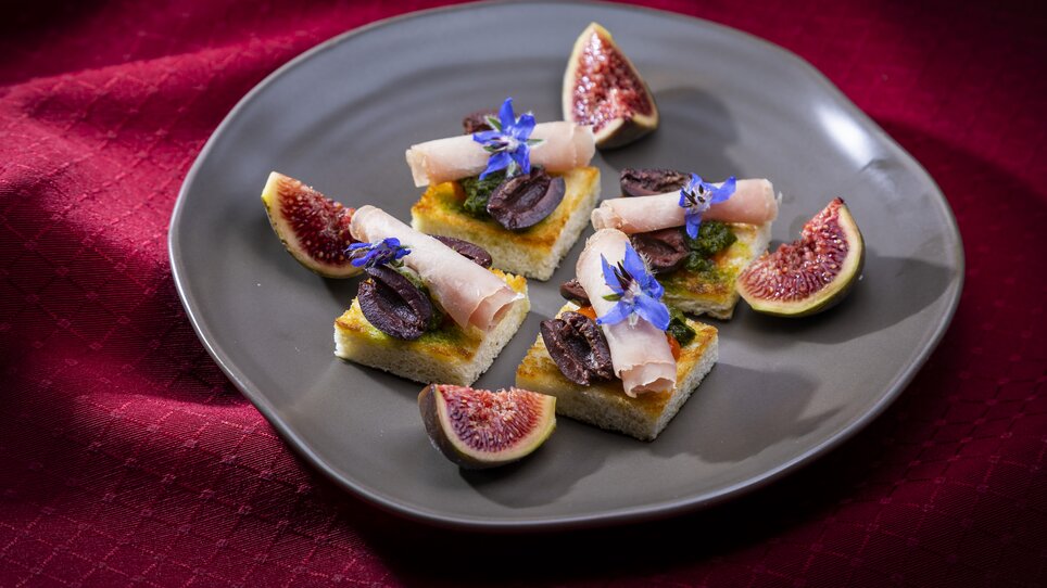 Un'elegante presentazione di piccoli bocconcini con prosciutto, olive e fichi, guarniti con fiori commestibili. | © Graz Tourismus - Werner Krug