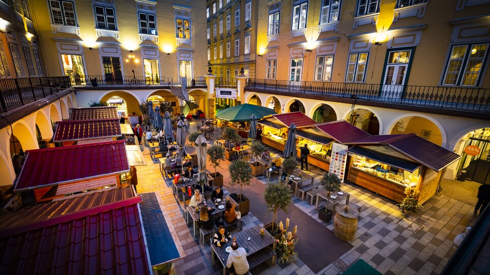 Gemütlicher Trüffelmarkt im Paradeishof mit beleuchteten Ständen und Gästen. Abendlich beleuchtet mit schönen Umgebungen. | © Graz Tourismus - Werner Krug
