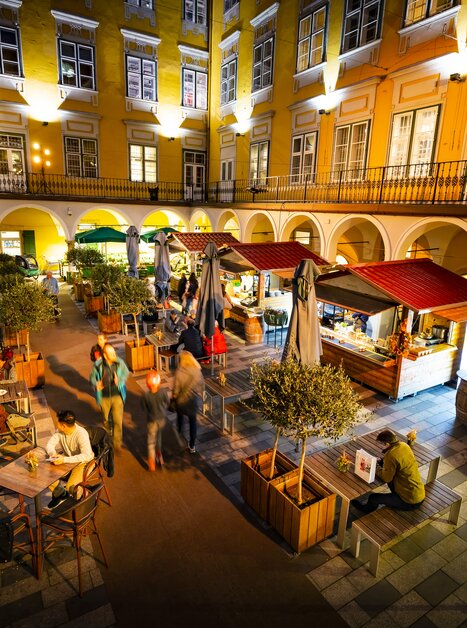 Abendliche Szene eines belebten Trüffelmarkts im Paradeishof in Graz mit Essensständen und Gästen. | © Graz Tourismus - Werner Krug
