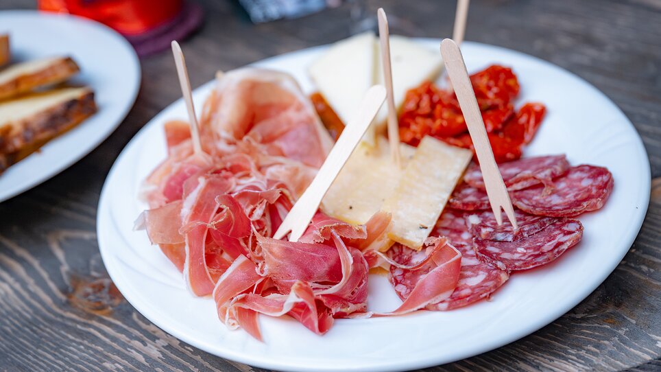 Ein Teller mit verschiedenen Wurstsorten, Käse und getrockneten Tomaten, serviert mit Holzstäbchen. | © 5komma5sinne - Rene Strasser