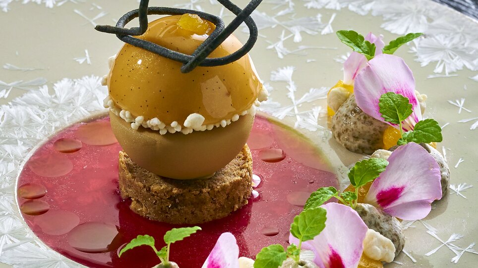 Ein kunstvolles Dessert, bestehend aus einer Fruchtkugel auf Keksboden, umgeben von Sauce und Deko. | © Bastian Knapp
