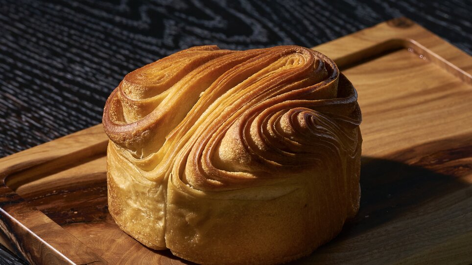 Ein frisch gebackenes Blätterteiggebäck - kunstvoll geformt - auf einem Holzbrett. | © Bastian Knapp