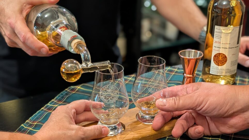 Two glasses are being filled with whiskey while two hands are ready. | © The Islay Whisky Chapter Austria