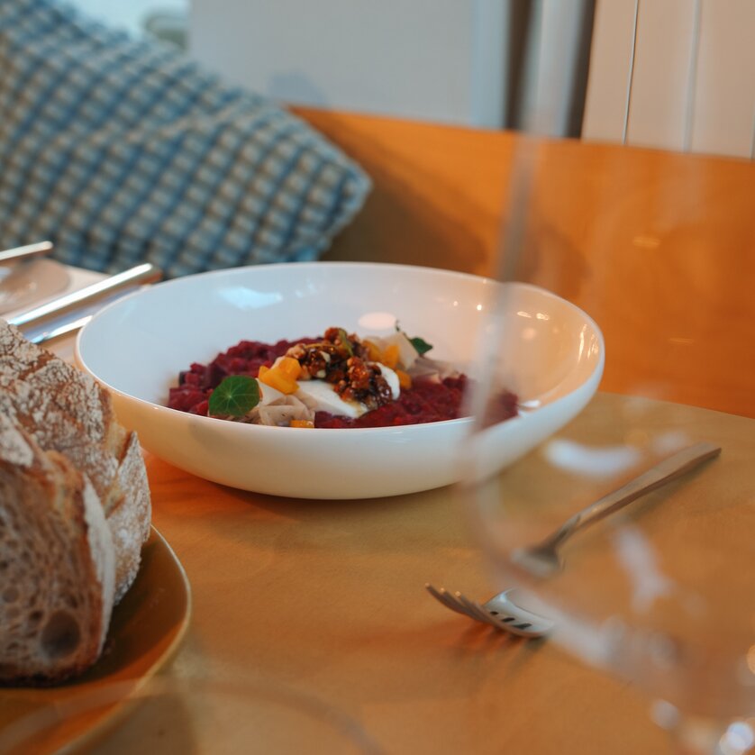 Eine Schüssel mit buntem Gericht und frischem Brot auf einem Tisch. Ganz in der Nähe steht ein Glas. | © Julia Riedesser - 1000things