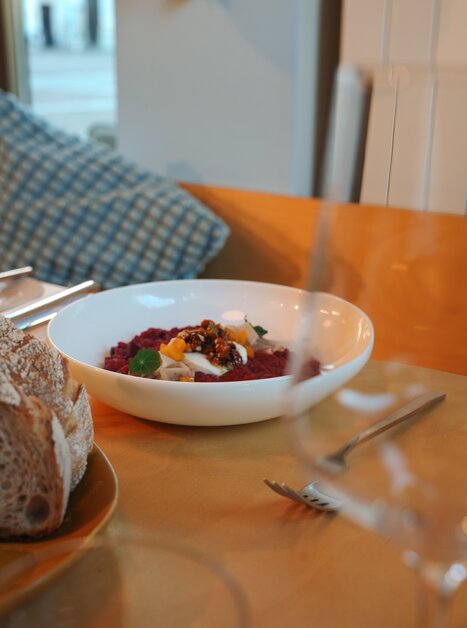 Eine Schüssel mit buntem Gericht und frischem Brot auf einem Tisch. Ganz in der Nähe steht ein Glas. | © Julia Riedesser - 1000things