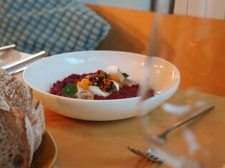 Eine Schüssel mit buntem Gericht und frischem Brot auf einem Tisch. Ganz in der Nähe steht ein Glas. | © Julia Riedesser - 1000things