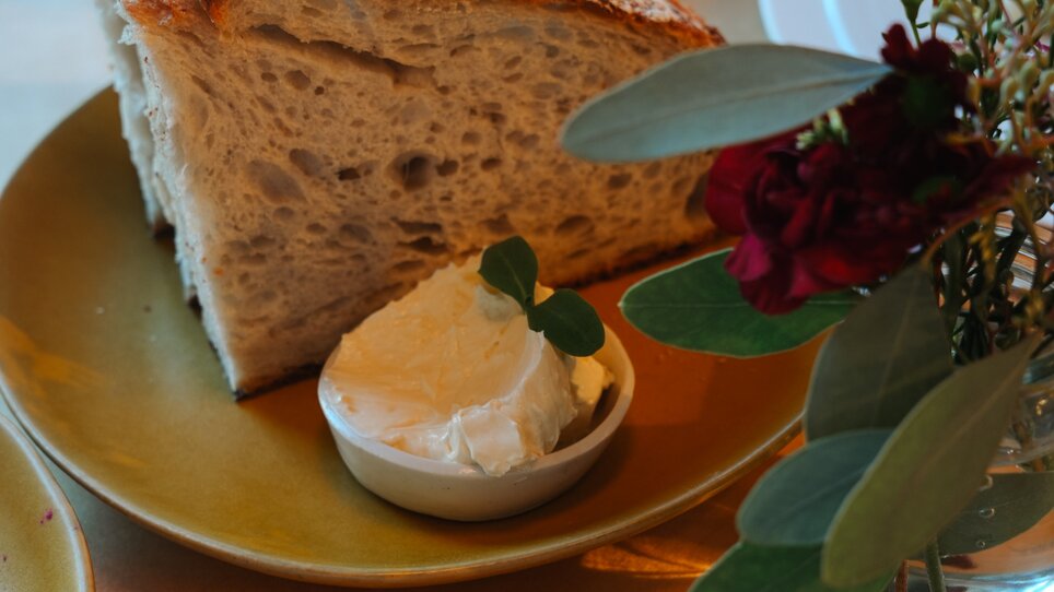 Ein Stück frisches Brot mit einer Portion Butter auf einem Teller. | © Julia Riedesser - 1000things