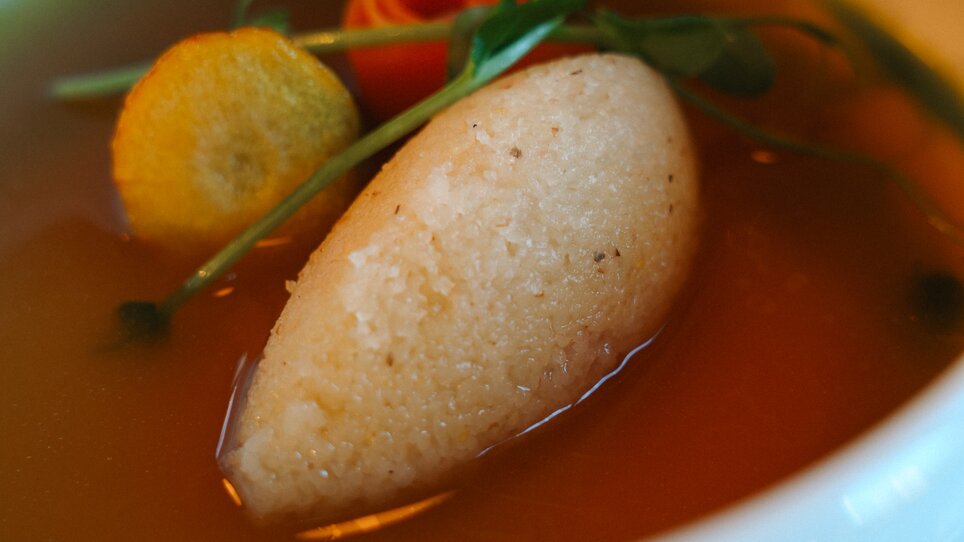 Eine klare Suppe mit einem Griesnockerl und Gemüse als Beilage in einer weißen Schale. | © Julia Riedesser - 1000things