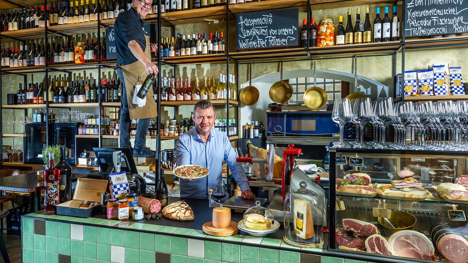 Due uomini in un ristorante, uno serve la pasta, l'altro tiene una bottiglia di vino. | © Paul Stajan
