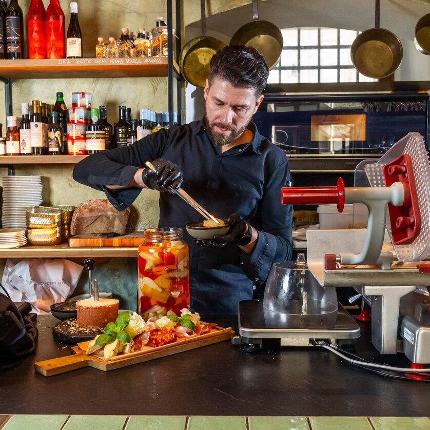 Ein Koch bereitet ein Gericht mit frischen Zutaten an einer Theke zu. | © Paul Stajan
