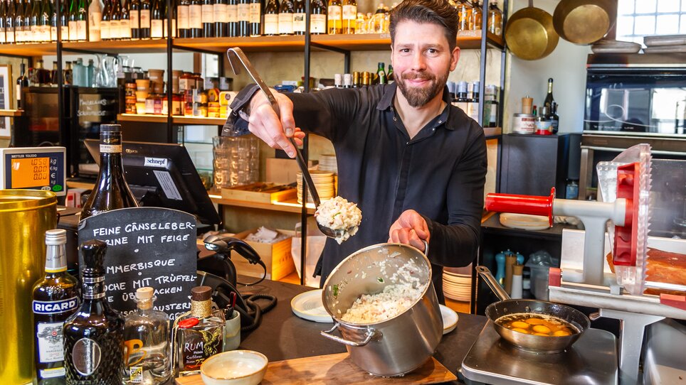 Uomo serve piatto in un ristorante con una scaffale di vini. | © Paul Stajan