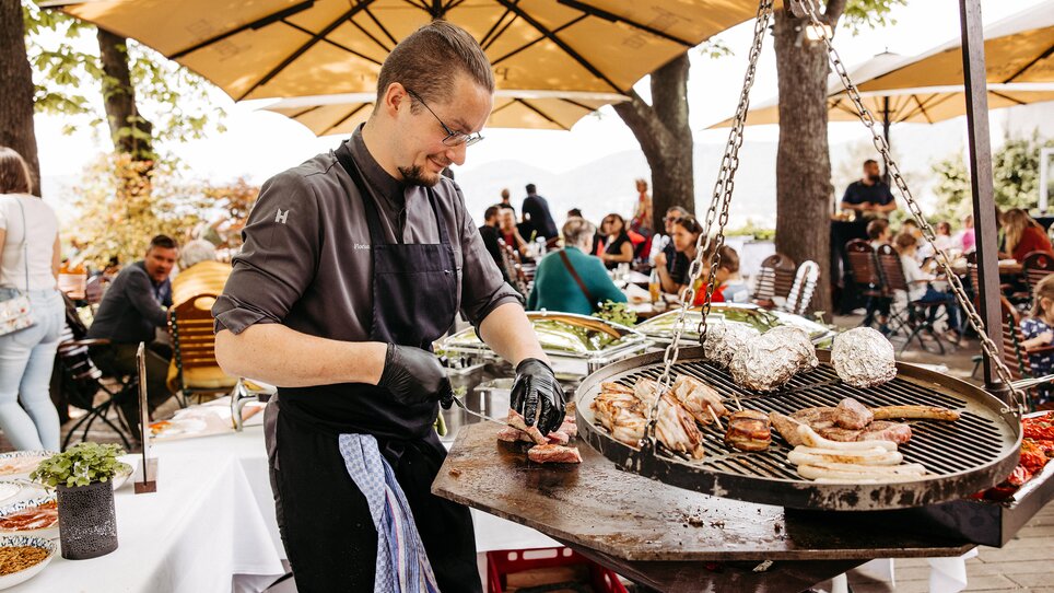 A chef grills meat and vegetables on a terrace outdoors. | © Benjamin Gasser