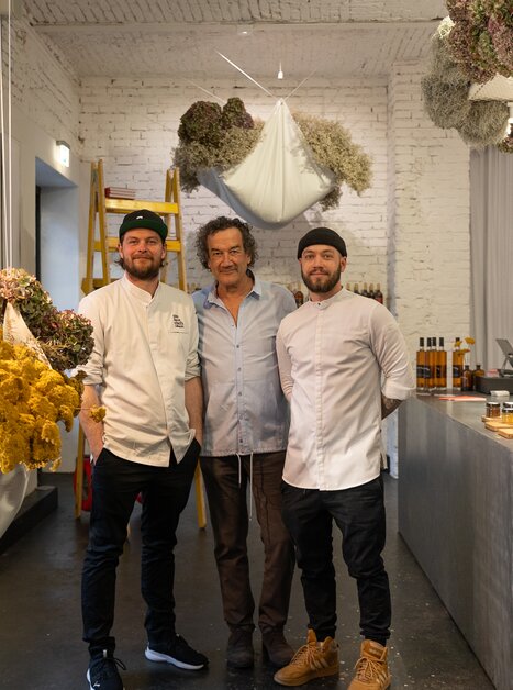 Drei Köche stehen in einem Gastronomieladen mit Trockenblumen und Produkten. | © Michael Kink