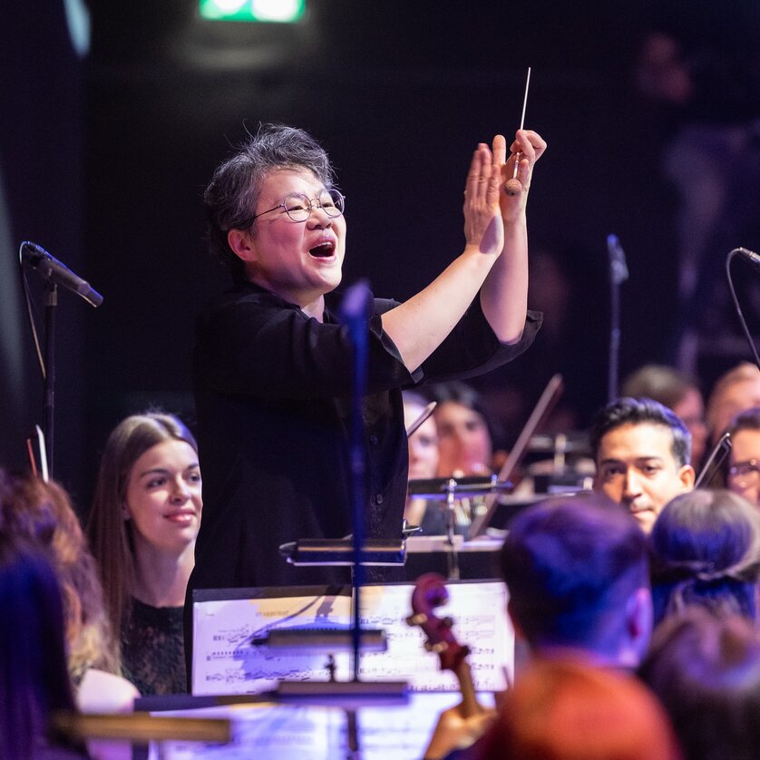 A conductor directs an orchestra as musicians attentively follow her cues. | © Nikola Milatovic