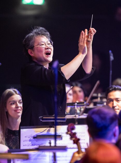 A conductor directs an orchestra as musicians attentively follow her cues. | © Nikola Milatovic