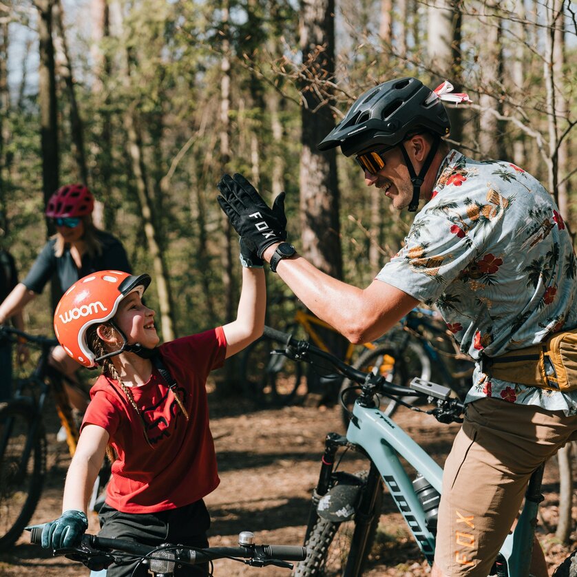 Ein Kind und ein Erwachsener freuen sich beim Mountainbiking. Im Hintergrund sind weitere Radfahrer zu sehen. | © Johannes Bitter