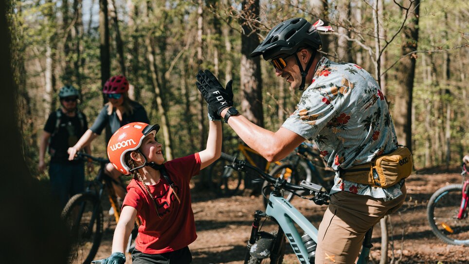 Ein Kind und ein Erwachsener freuen sich beim Mountainbiking. Im Hintergrund sind weitere Radfahrer zu sehen. | © Johannes Bitter