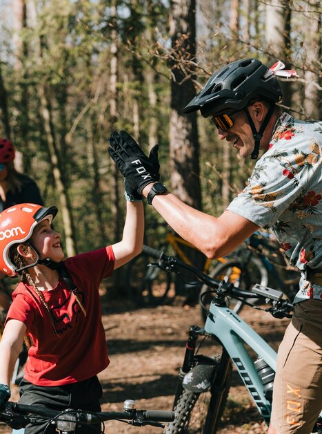 Ein Kind und ein Erwachsener freuen sich beim Mountainbiking. Im Hintergrund sind weitere Radfahrer zu sehen. | © Johannes Bitter