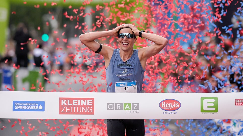 A runner celebrates victory at the Graz marathon, surrounded by confetti. | © GEPA
