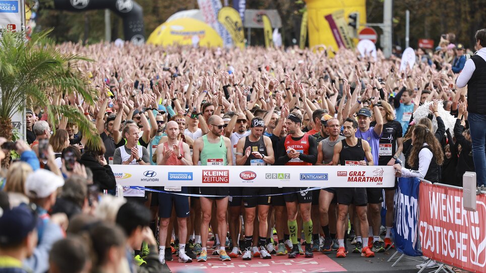 Runners and spectators at the start of the Graz Marathon, many hands in the air. | © GEPA