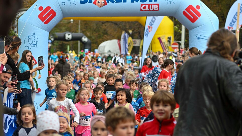 A large crowd of children running under a colorful finish arch. | © GEPA