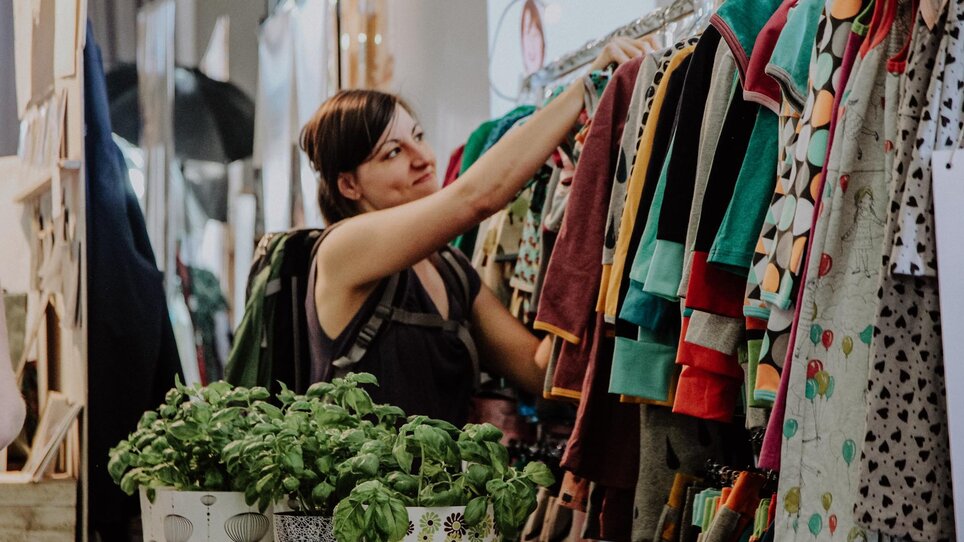 Eine Frau betrachtet Kleidung an einem Stand auf dem Kunst- und Designmarkt. | © Kunst- und Designmarkt