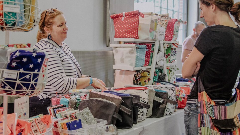 Eine Verkäuferin zeigt Taschen auf einem Kunst- und Designmarkt. | © Kunst- und Designmarkt