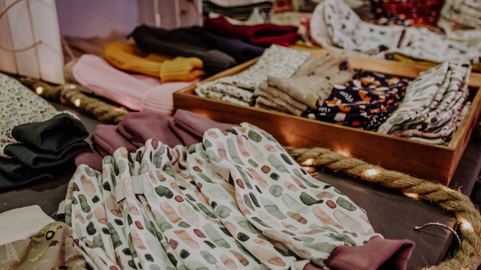 Bunte Stoffe und Kleidung auf einem Tisch beim Kunst- und Designmarkt. | © Kunst- und Designmarkt