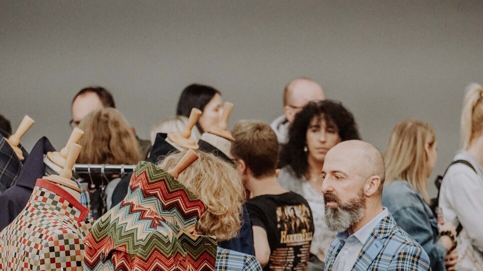 Besucher auf einem Kunst- und Designmarkt mit bunten Kleidungsstücken.