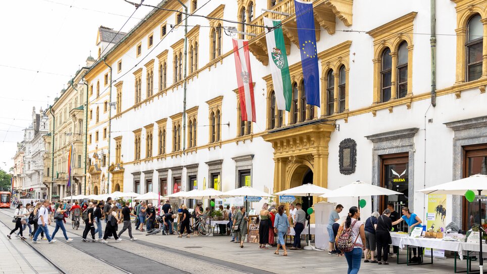 Colorful market stalls and people in Graz in front of historic architecture. | © Harry Schiffer