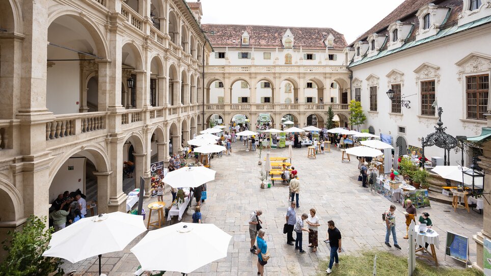 Visitors enjoy a market in the courtyard with white umbrellas. | © Harry_Schiffer