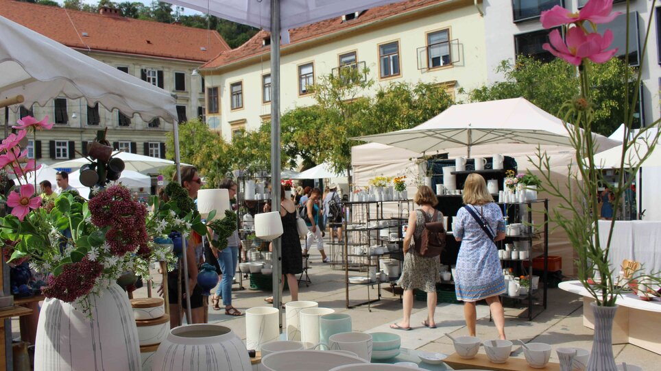 Besucher erkunden Töpfermarkt mit Töpferwaren und Pflanzen.