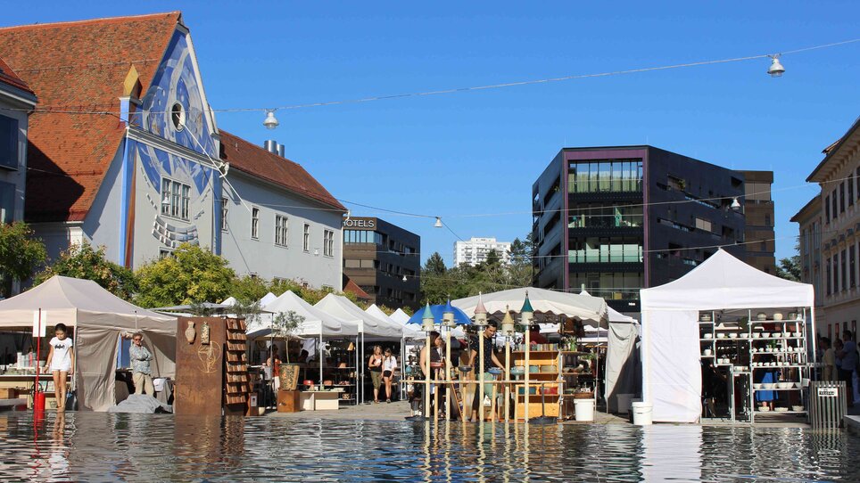 Blick auf den Töpfermarkt mit Marktständen und blauer Himmel in Graz.