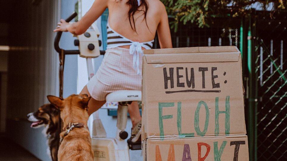 Frau mit Hund in Hof mit Schild für Flohmarkt von 8 bis 19 Uhr. | © Stella