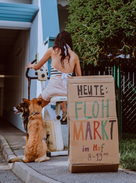 Donna con cane nel cortile con cartello per mercatino delle pulci dalle 8 alle 19. | © Stella
