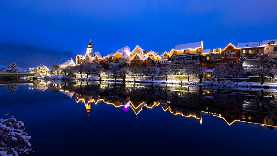 Beleuchtete Gebäude in Frohnleiten reflektieren im Wasser, umgeben von Schnee. | © Region Graz - Harry Schiffer