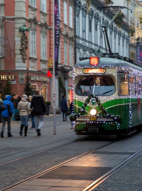 A festively lit tram is passing through Graz, surrounded by people and decorated shops. | © Graz Tourismus - Harry Schiffer