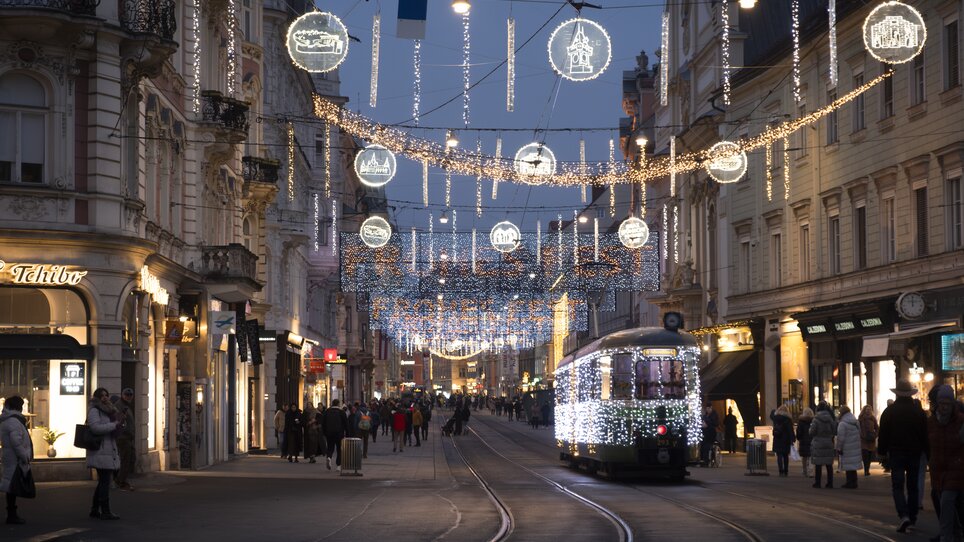 Illuminated street in Graz with a tram and festive decorations. | © Vincent Croce