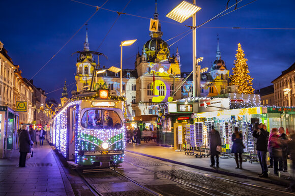 Un tram dell'Avvento illuminato a Graz, circondato da una scena invernale e un mercato di Natale. | © Graz Tourismus - Werner Krug