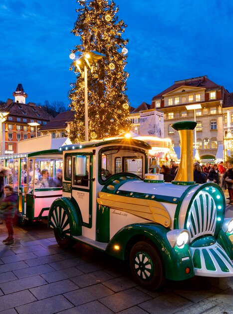 A festive city view of Graz during Advent, with a lit-up advent train driving through the streets. | © Graz Tourismus-Harry Schiffer